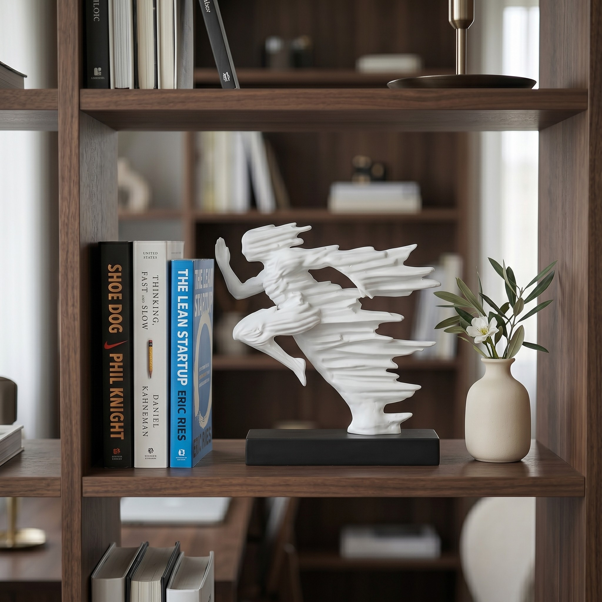 White abstract momentum sculpture styled on a modern wooden bookshelf between business books and a small vase