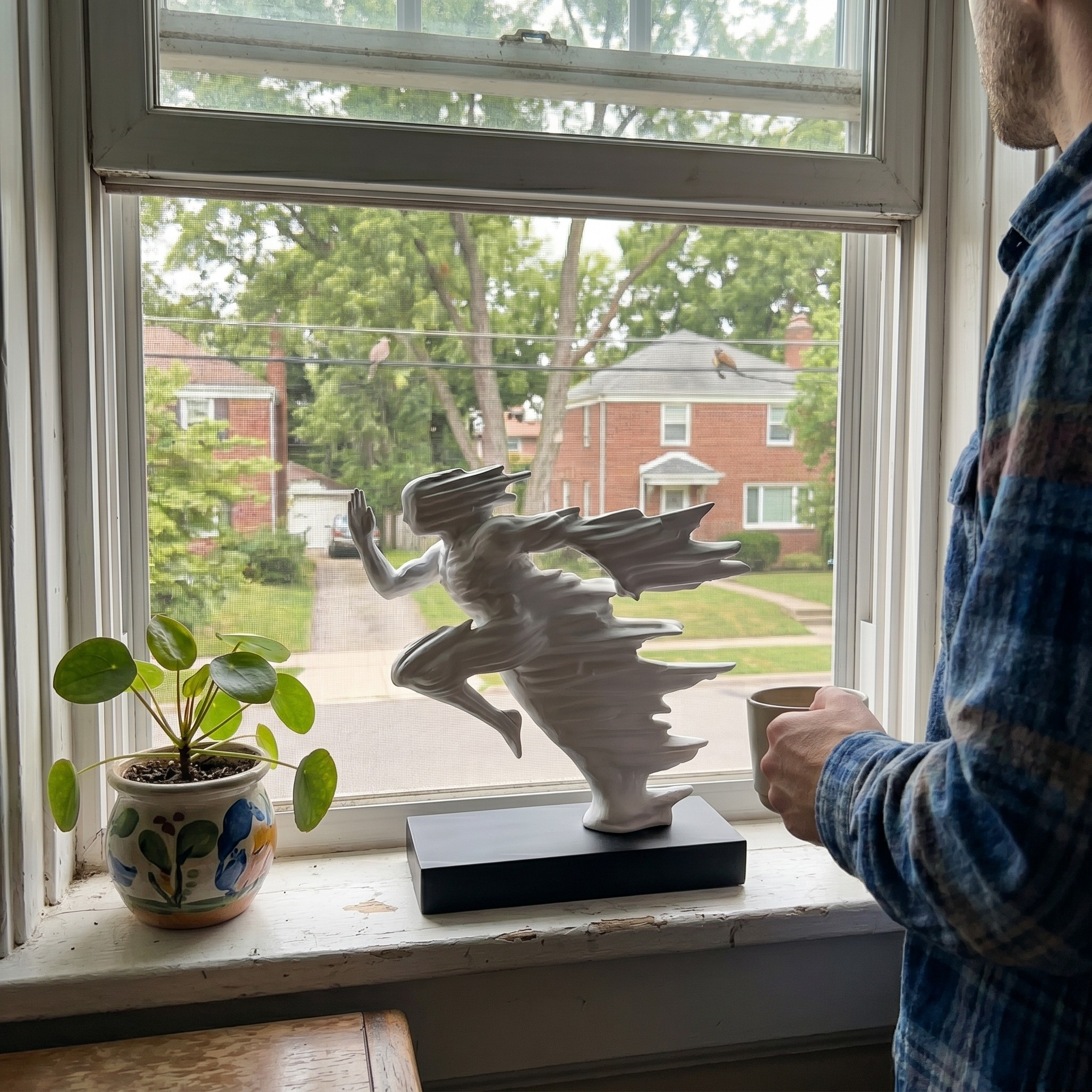 White minimalist running sculpture placed on a wide window sill with natural sunlight and a green garden view