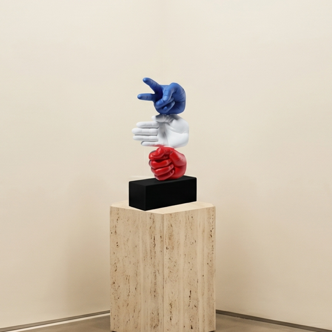 Sculpture of three hands in different colors on a wooden pedestal against a beige wall.