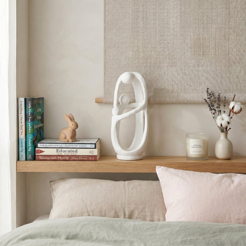 Decorative shelf with books, a rabbit figurine, a white sculpture, and a candle on a bed.