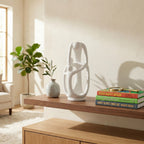An abstract matte white "INFINITE" family sculpture on a walnut shelf, showing three interlocking stylized figures forming a continuous loop.